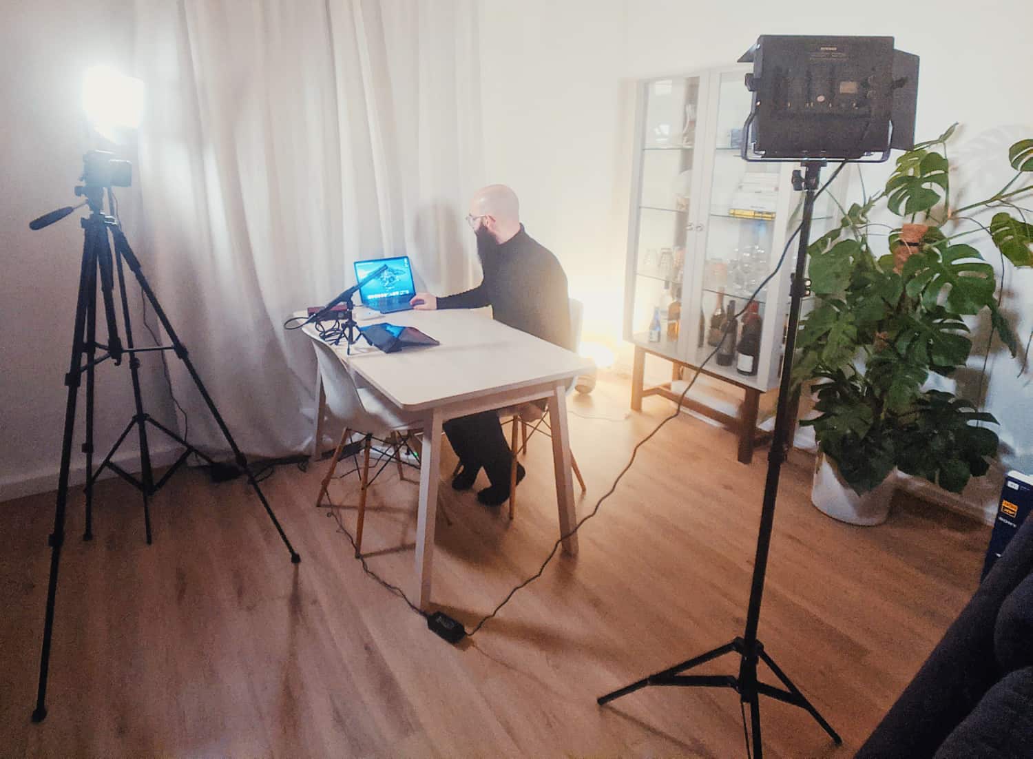 Glatzköpfiger Mann produziert Content an einem Tisch mit Laptop, umgeben von professionellem Videoequipment - Einblick in die Arbeit eines Glatzen-Influencers