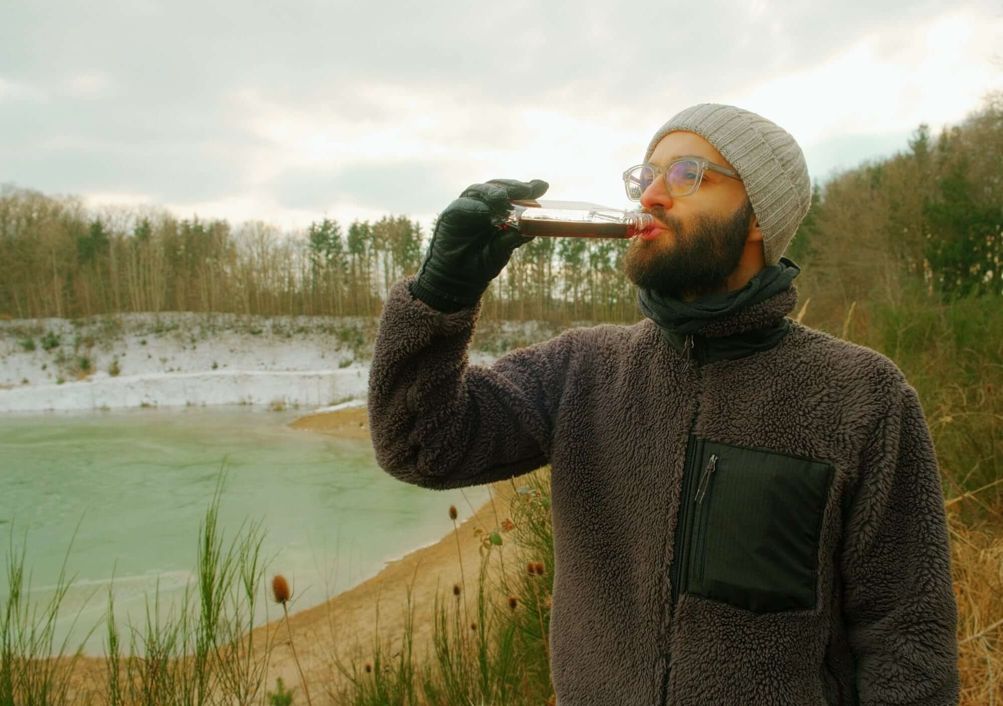 Selbstbewusster Glatzenträger genießt Digital Detox am türkisfarbenen Waldsee, authentischer Moment in Winterkleidung bei Selbstfindung in der Natur