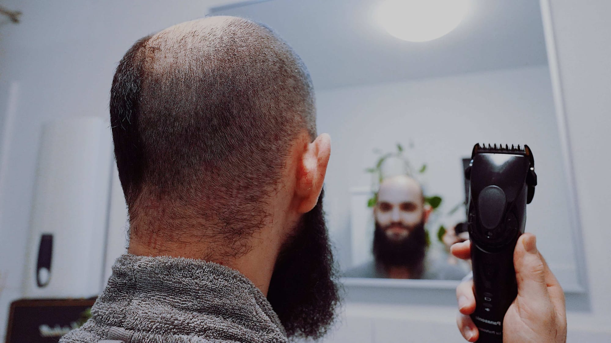 Mann rasiert sich vor dem Spiegel den Kopf, bewusste Entscheidung für Glatze bei Haarausfall