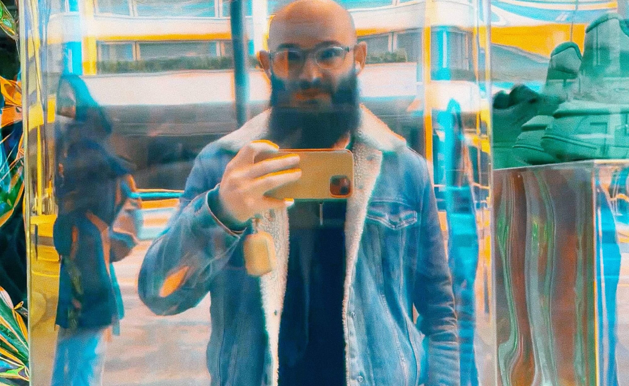 Mann mit Glatze und Bart in Jeansjacke, Spiegelung, urbaner Stil, Glatze als Statement für Selbstbewusstsein