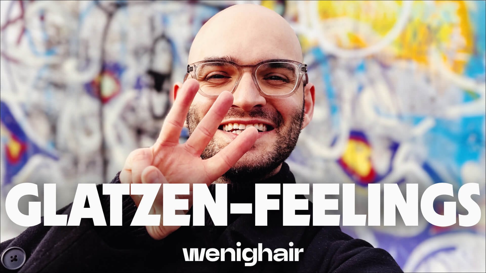 Selbstbewusster Mann mit Glatze zeigt lächelnd wenighair-Zeichen, transparente Brille vor bunter Graffiti-Wand