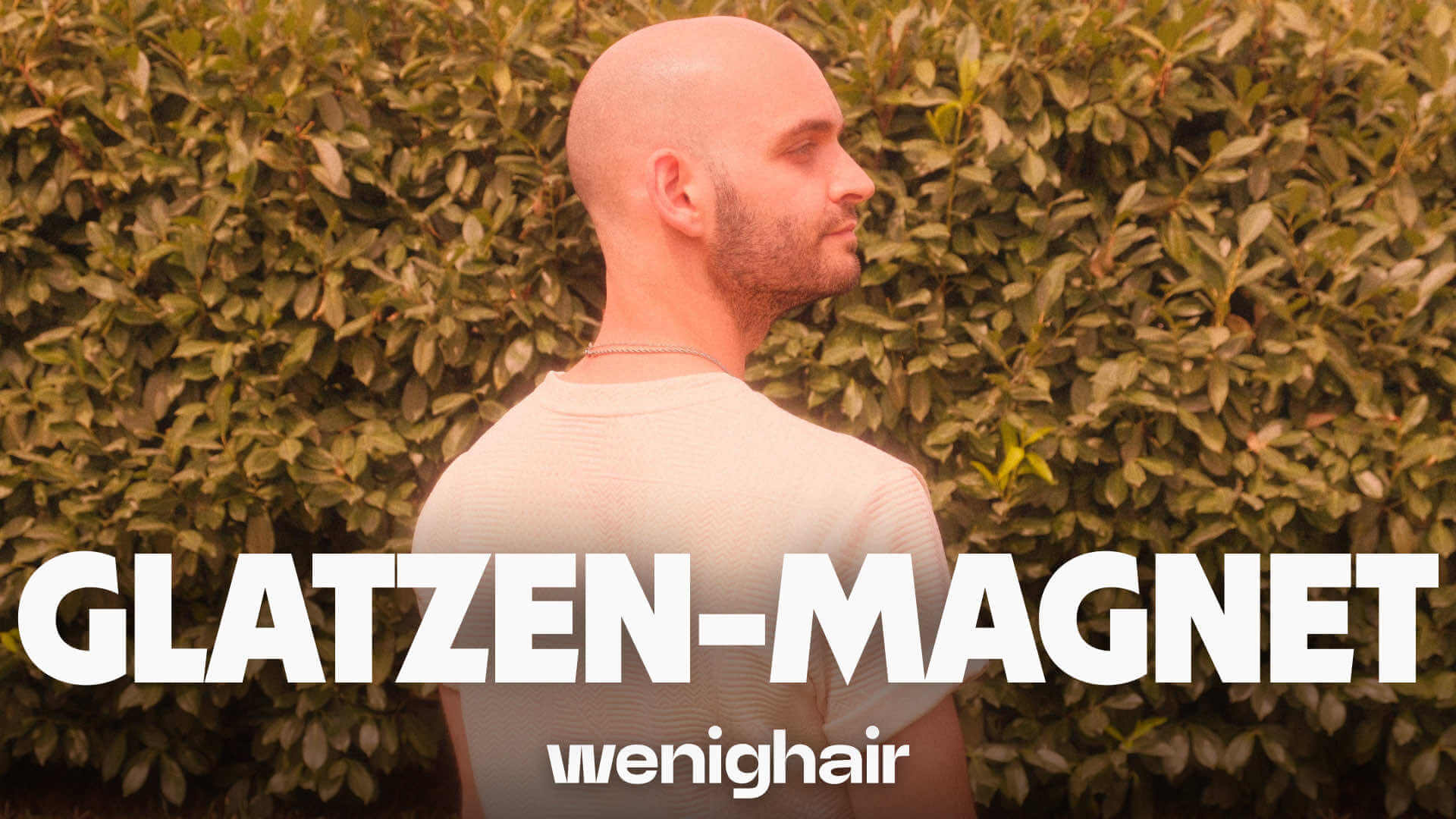 Mann mit Glatze und weißem Shirt vor Hecke, Text „GLATZEN-MAGNET“ Symbol für selbstbewusstes Auftreten mit Glatze