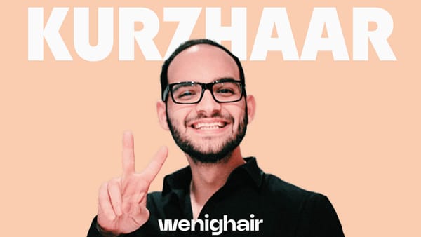 Lächelnder Mann mit Kurzhaarfrisur und Brille zeigt ein Peace-Zeichen. Kurz Haar Frisuren Männer.